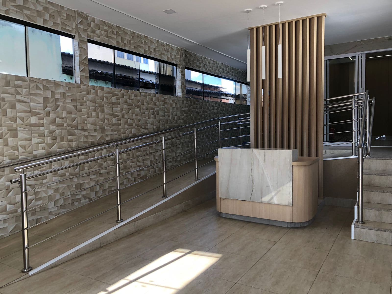 Hall de entrada do centro clínico, com recepção em mármore e rampa de acesso